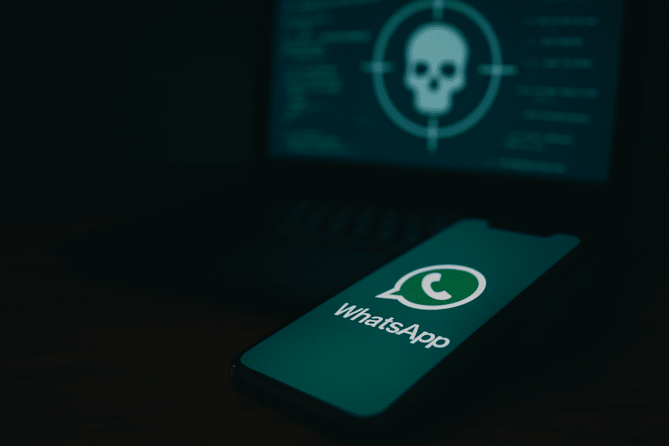 Maverick: Imagem realista mostra um smartphone com o logotipo do WhatsApp em destaque diante de um laptop com tela exibindo código e símbolo de ataque hacker, representando o trojan bancário Maverick usado em campanhas no Brasil.