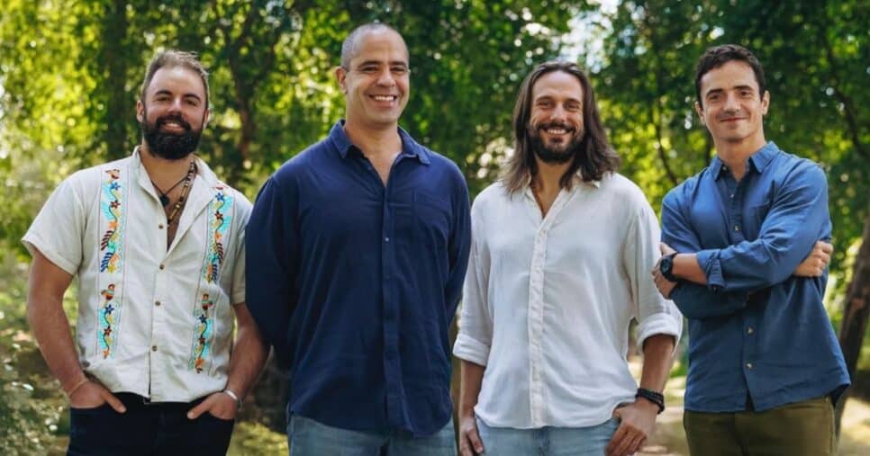 A imagem mostra quatro pessoas em pé, em um ambiente externo com bastante vegetação ao fundo, sugerindo um parque ou área arborizada. A cena parece informal e descontraída. (Diva e Ginga)