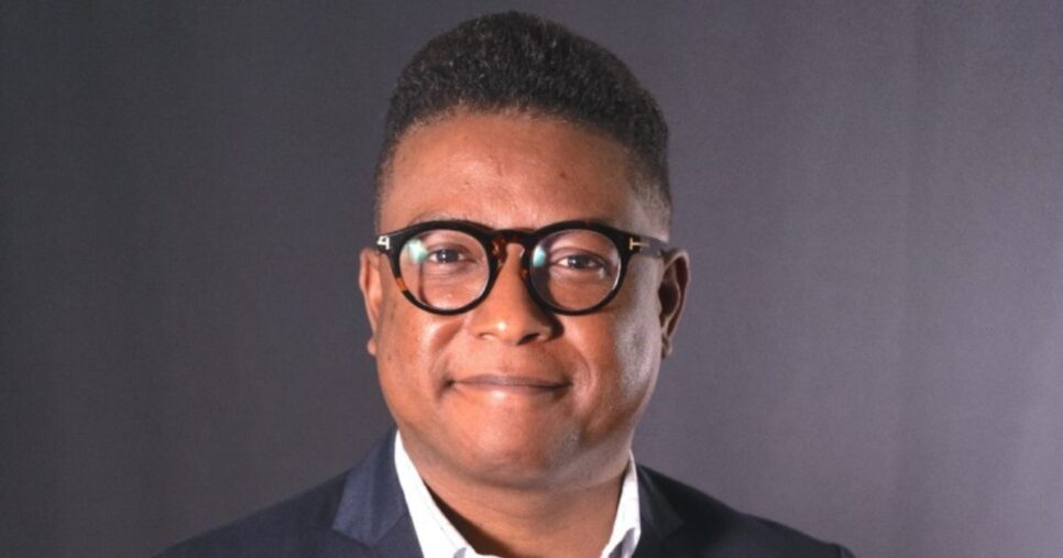 A imagem mostra uma pessoa vestindo traje formal, com uma camisa clara e um blazer escuro, em frente a um fundo neutro, sugerindo um cenário corporativo ou profissional. (Coca-Cola)