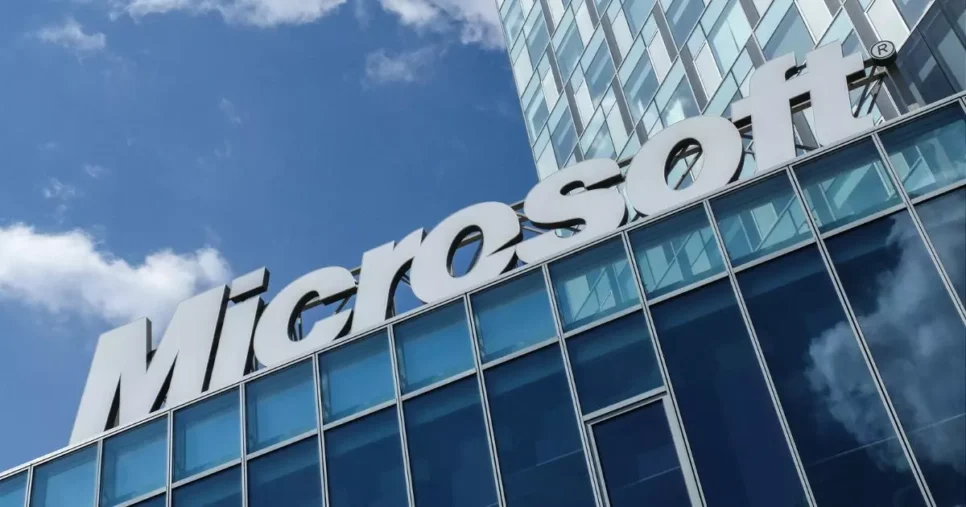 A imagem mostra a fachada de um edifício corporativo moderno, com destaque para o logotipo da Microsoft em letras grandes e brancas, posicionado na parte superior da estrutura.