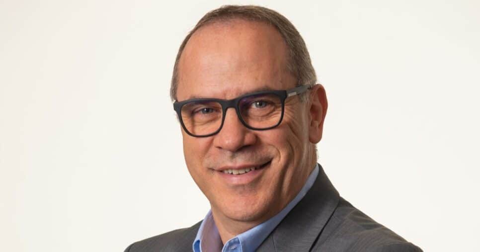 Ricardo Emmerich, diretor-geral da HPE Brasil, usando terno cinza, camisa azul clara e óculos escuros de armação grossa, sorrindo em fundo claro.
