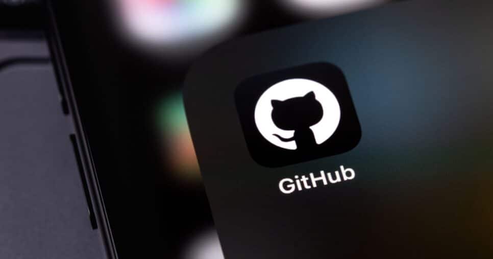 Logo do GitHub exibido na tela de um dispositivo móvel, com o icônico ícone de um gato em silhueta branca dentro de um círculo preto. O fundo desfocado destaca cores suaves, criando um ambiente tecnológico e minimalista, Github, Teki, Microsoft