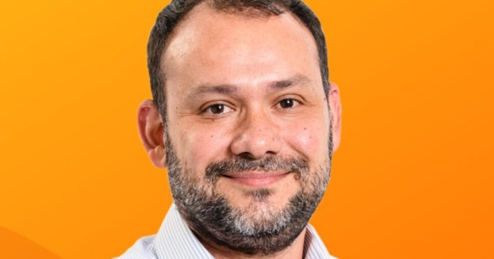 Pessoa vestindo uma camisa social listrada em tom claro, posicionada diante de um fundo laranja vibrante que ocupa toda a composição. A imagem transmite um clima moderno e energético devido ao contraste entre as cores. (Microsoft, Rodrigo Caserta)