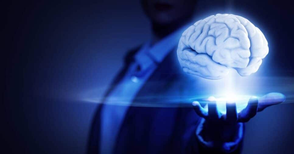 Pessoa em ambiente escuro com a mão estendida, segurando holograficamente um cérebro iluminado em azul, simbolizando superinteligência artificial, futuro