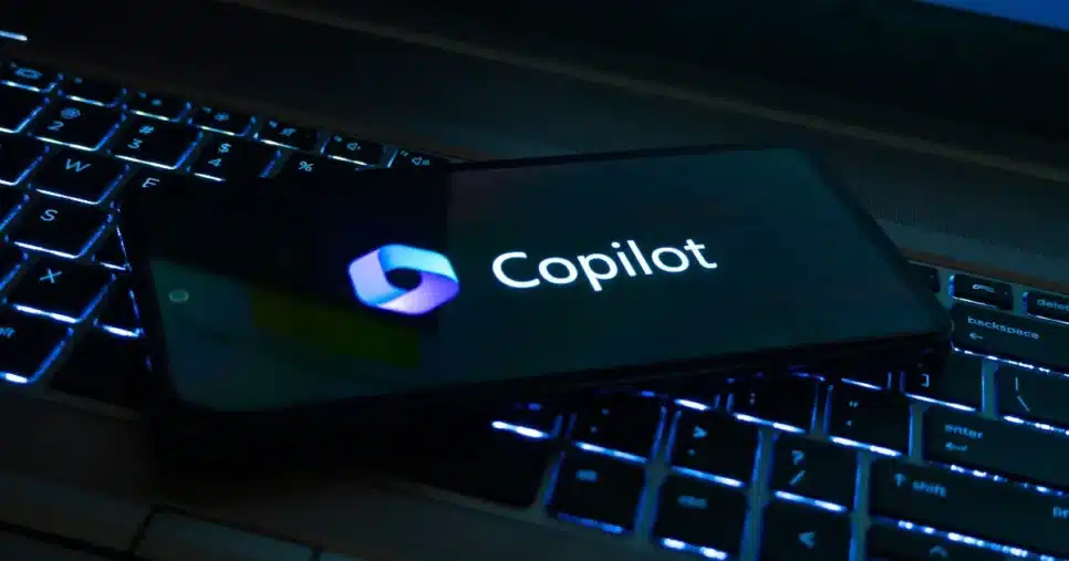 Imagem de um smartphone exibindo o logotipo e o nome 'Copilot', da Microsoft, posicionado sobre um teclado retroiluminado, representando inovação e integração tecnológica. (microsoft) (copilot)